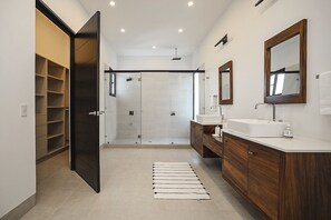 A modern bathroom with a walk-in shower, two sinks, wooden cabinets, and a large mirror.