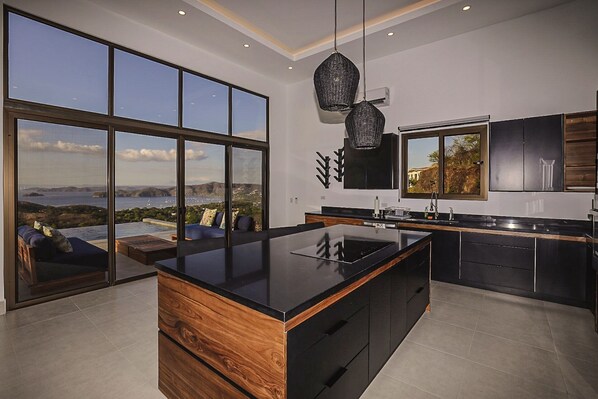 A modern kitchen with large windows, a central island, and a view of the sea.