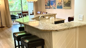 Uma cozinha com bancada de granito, pia e banquetas de bar. Há duas luminárias pendentes sobre a bancada.