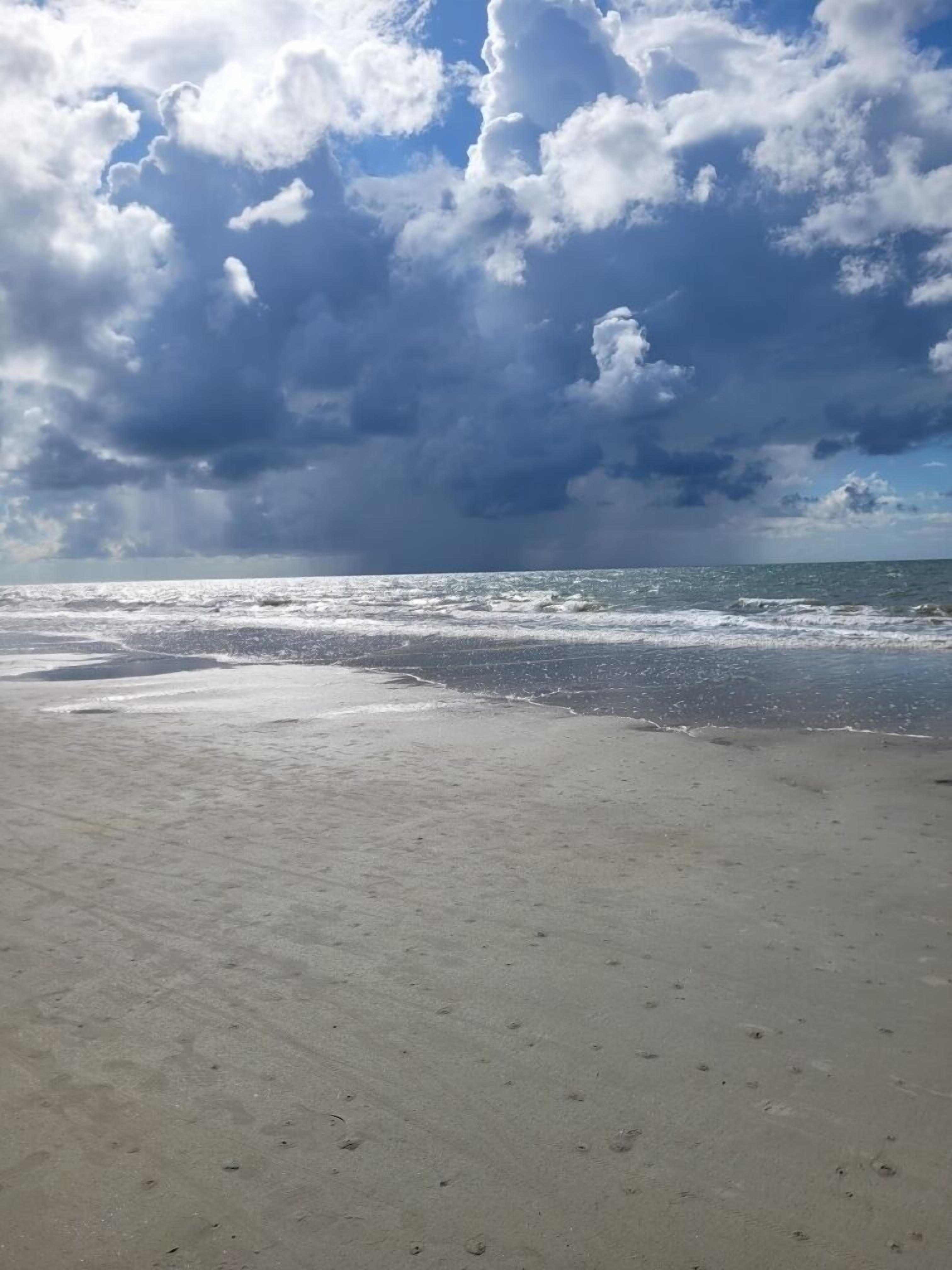 Une plage avec un rivage sablonneux et une vue sur l’océan, sous un ciel nuageux.