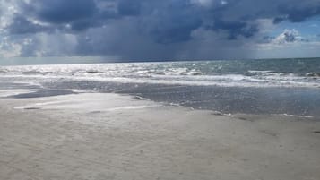 Une plage avec un rivage sablonneux et une vue sur l’océan, sous un ciel nuageux.