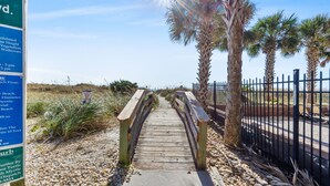 A wooden boardwalk leading to a beach with palm trees and a fence.