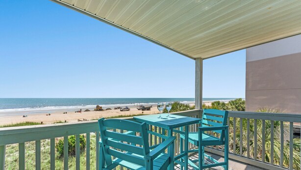 A balcony with a view of the beach, a table, and two chairs.