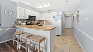 A modern kitchen with white cabinets, a central island with stools, a microwave, and a refrigerator.