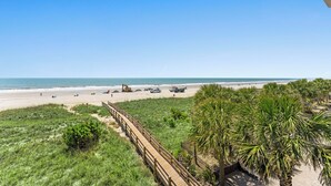 A beach view with a wooden boardwalk, palm trees, and beach activities.