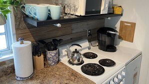 Una cocina con estufa, microondas y repisas con platos y vasos.