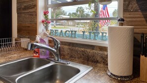 Una cocina con un lavamanos de acero inoxidable, una ventana con vista a un barrio y un letrero que dice 'BEACH LIFE'.