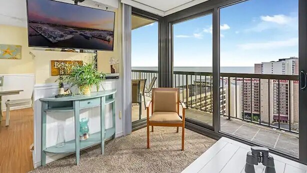 A modern living room with a large TV, a sofa, a chair, and a balcony with a city view.