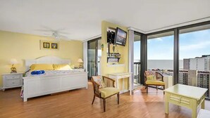 A hotel room with a bed, a desk, a chair, and a large window offering a city view.