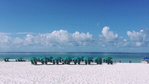 A beach with rows of green umbrellas and beach chairs, a clear blue sky, and the ocean in the background. - Golf Cart - 2 min to Beach - Pool - Walk to Shops & Dining! (Santa Rosa Beach)