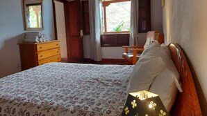 A bedroom with a bed, a dresser, a chair, a window with curtains, and a lamp. - Rural House Tía Rita La Gomera (Vallehermoso)