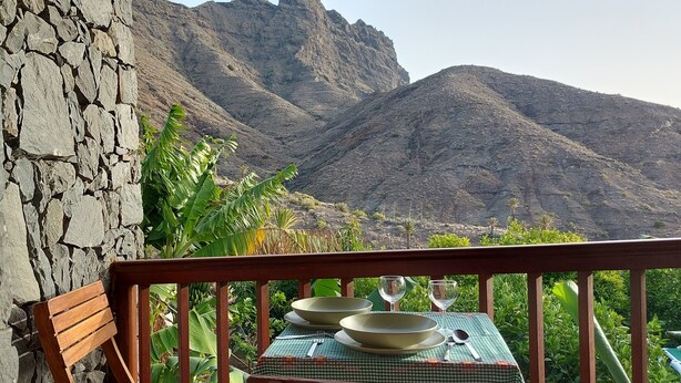 A balcony with a table set for two, overlooking a mountainous landscape. - Rural House Tía Rita La Gomera (Vallehermoso)