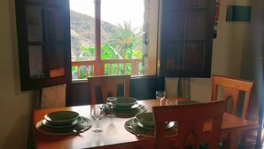 A dining table set with plates, glasses, and a window with a view of greenery and mountains. - Rural House Tía Rita La Gomera (Vallehermoso)