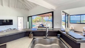 A modern kitchen with a large sink, a flat-screen TV, and a view of a pool and ocean. - Villa Zen – Sea View Villa with Pool & Jacuzzi (Cul-de-Sac)