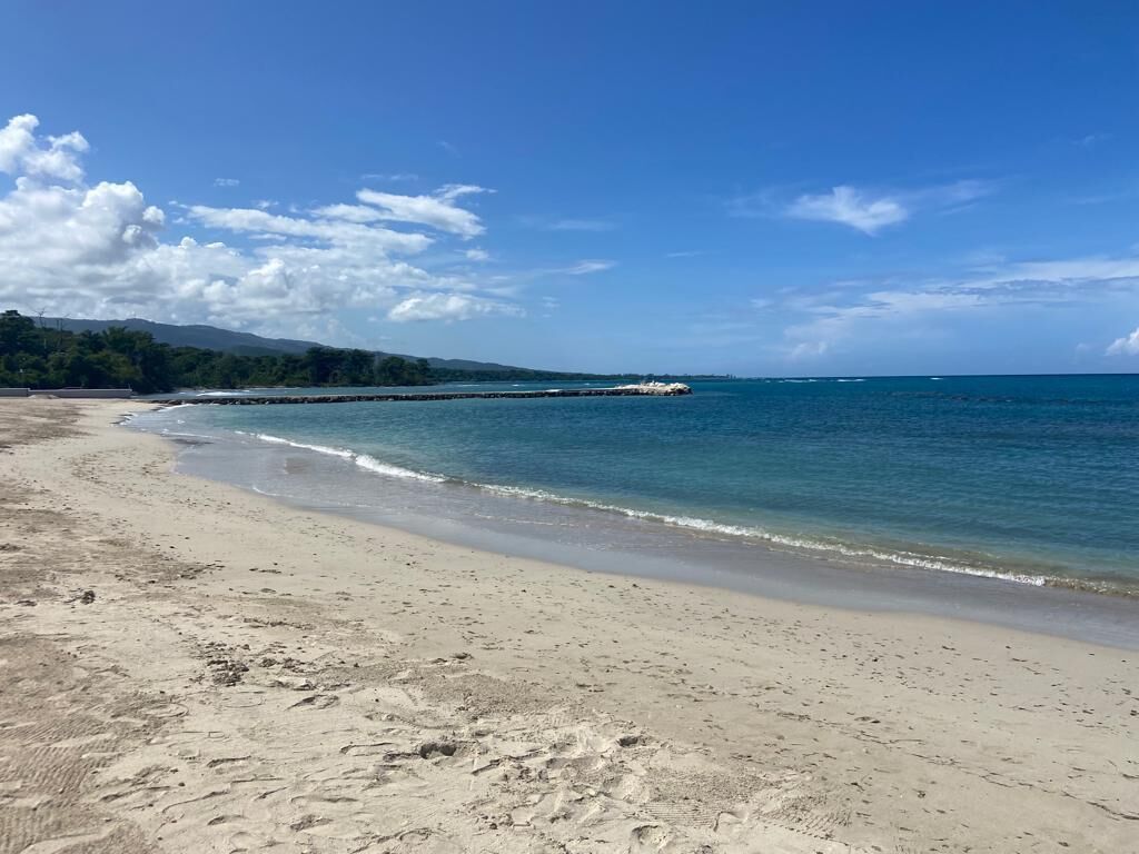 A beach with clear blue water, sandy shore, and distant mountains.
