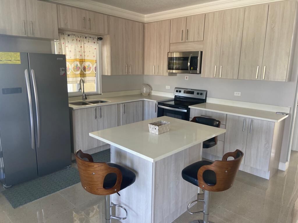 A modern kitchen with light wood cabinets, stainless steel appliances, and a central island with two bar stools.