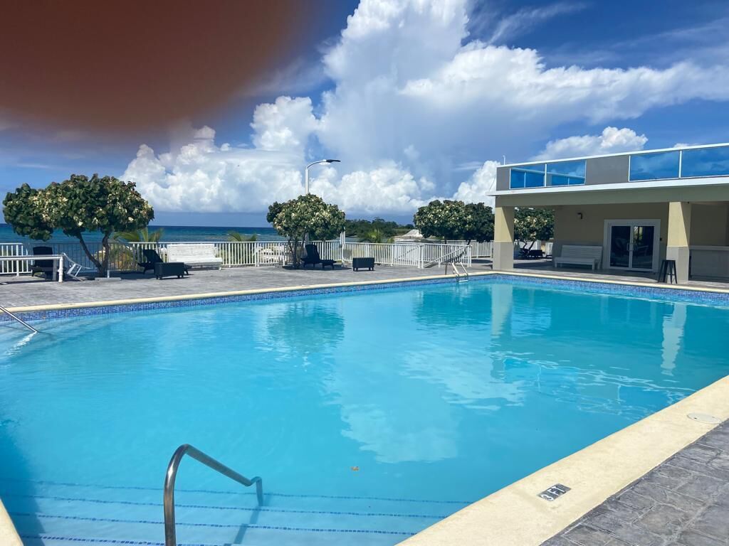 Ein Pool mit freiem Blick auf den Ozean, ein überdachter Sitzbereich und ein Gebäude mit flachem Dach.