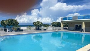 A swimming pool with a clear view of the ocean, a covered seating area, and a building with a flat roof. - Modern, chic waterfront 3-bedroom villa w/ pool (Saint Ann's Bay)