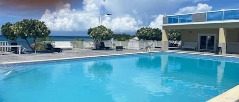 Una piscina con vistas despejadas al océano, un área de descanso cubierta y un edificio con tejado plano.