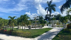 A landscaped area with a fountain, palm trees, and a paved walkway. - Modern, chic waterfront 3-bedroom villa w/ pool (Saint Ann's Bay)