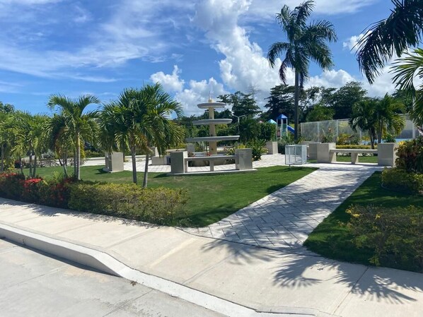 A landscaped area with a fountain, palm trees, and a paved walkway.