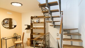 A modern interior with a spiral staircase, a round mirror, a glass table, and a wooden chair.