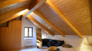 A bedroom with a sloped ceiling, wooden beams, a bed, a dresser, and a window.