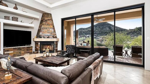 A modern living room with a fireplace, leather sofa, and a large sliding glass door leading to an outdoor patio. - 5 Star INFINITY POOL Saguaro Mountain Desert House (Scottsdale)