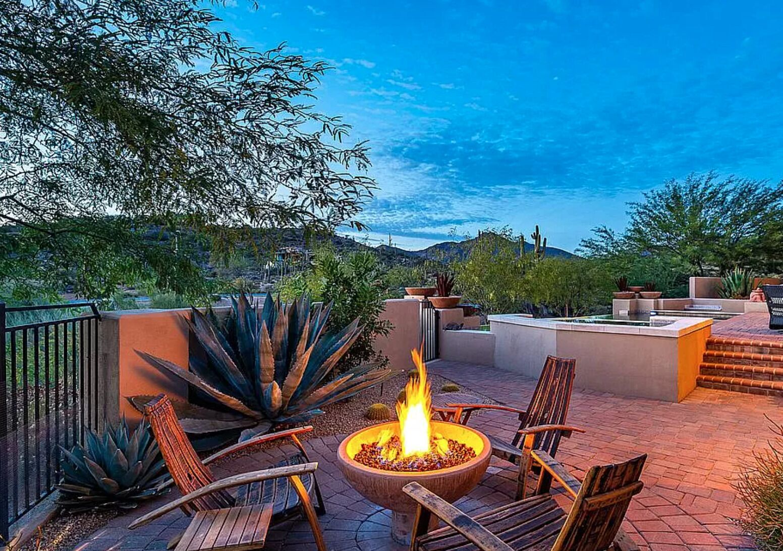 An outdoor patio with a fire pit, wooden chairs, and a view of the surrounding landscape.