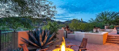 An outdoor patio with a fire pit, wooden chairs, and a view of the surrounding landscape.