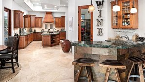 A spacious kitchen with wooden cabinets, a central island, and a dining area with a table and chairs. - 5 Star INFINITY POOL Saguaro Mountain Desert House (Scottsdale)