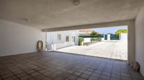 An empty room with tiled flooring, a visible ceiling light, and a view of a courtyard with a gate and greenery.