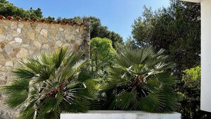 Un muro de piedra con tejado de baldosas, palmeras y una jardinera de hormigón blanco.