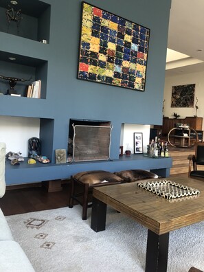 A living room with a blue accent wall, a large abstract painting, a fireplace, and a coffee table with a woven coaster set.