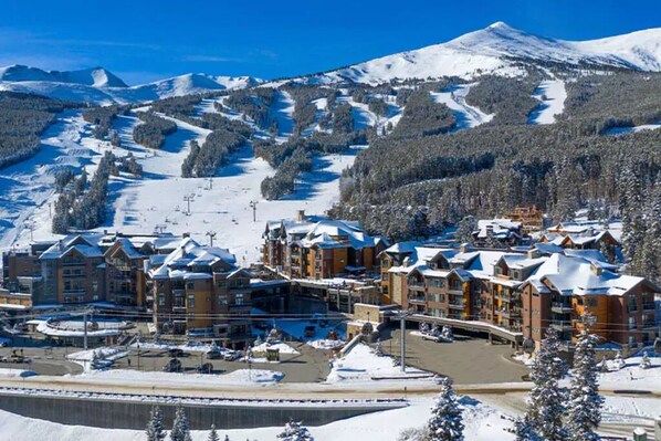 A snow-covered mountain resort with multiple buildings, ski slopes, and a parking area. - Ski in Ski out Breckenridge Grand Colorado 8- Studio sleeps 4 Mar 30-Apr 6, 2024 (Breckenridge)