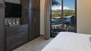 Una camera da letto con un letto grande, una TV montata su una cassettiera in legno scuro e vista su una montagna innevata attraverso una porta scorrevole in vetro.