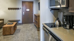Una cucina compatta con forno a microonde, macchina del caffè e lavastoviglie. Nell’area soggiorno, una panca in legno e un piccolo tavolo.