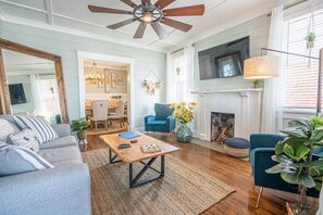 Ein geräumiges Wohnzimmer mit Deckenventilator, Kamin und Wand-Fernseher.