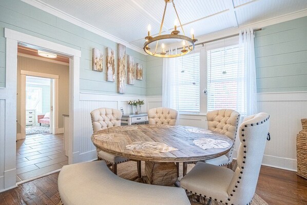A dining room with a round wooden table, six upholstered chairs, and a chandelier.