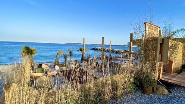 Ein Restaurant direkt am Strand mit Terrassenplätzen und Meerblick, das rustikale Holzbauten und natürliche Vegetation zeigt.