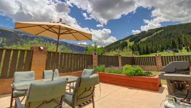 Un patio exterior con una mesa, sillas, una parrilla y vistas a un paisaje montañoso.
