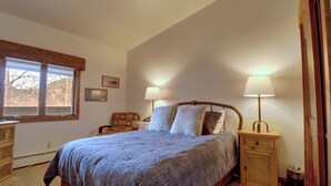 Un dormitorio con una cama grande, dos mesitas de noche, un ventanal y vistas a árboles.