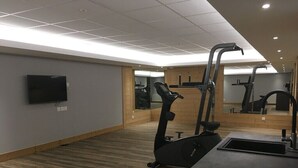 Et fitnessrum med trægulv, træningsudstyr, et fjernsyn og et spejl.