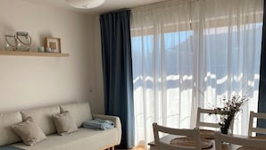 Un salon avec un canapé, une table à manger et des chaises, un tapis bleu et un luminaire au plafond.