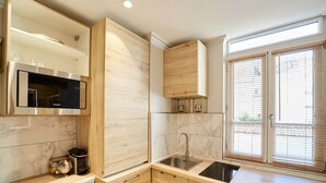Una cucina moderna con forno a microonde integrato, lavello, pensili in legno e una finestra con persiane.