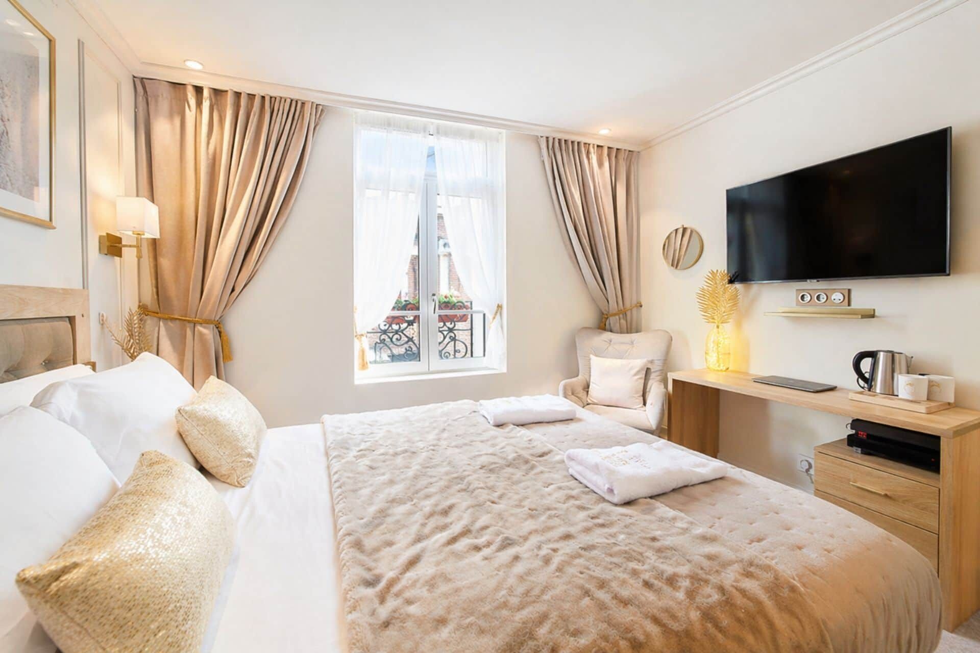 Une chambre d’hôtel avec un grand lit, une télévision, un bureau avec un ordinateur et une fenêtre donnant sur un immeuble.