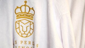 Un tessuto bianco con un ricamo dorato e il testo 'S PERL S IENOIS'.