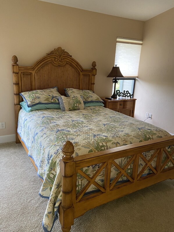 Un dormitorio con una cama de madera, ropa de cama estampada con motivos florales, una mesita de noche y una ventana con persianas.