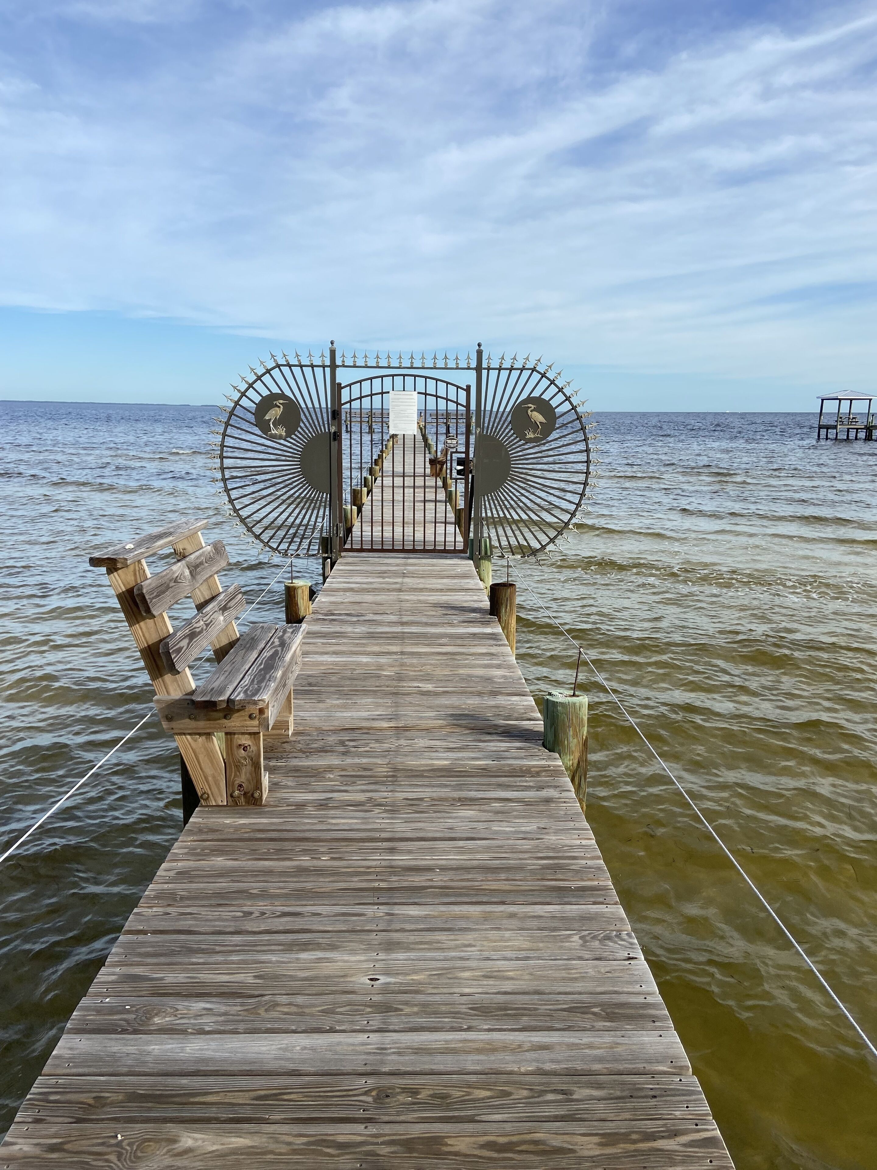 A wooden pier leading to a gated entrance with a bench on each side.