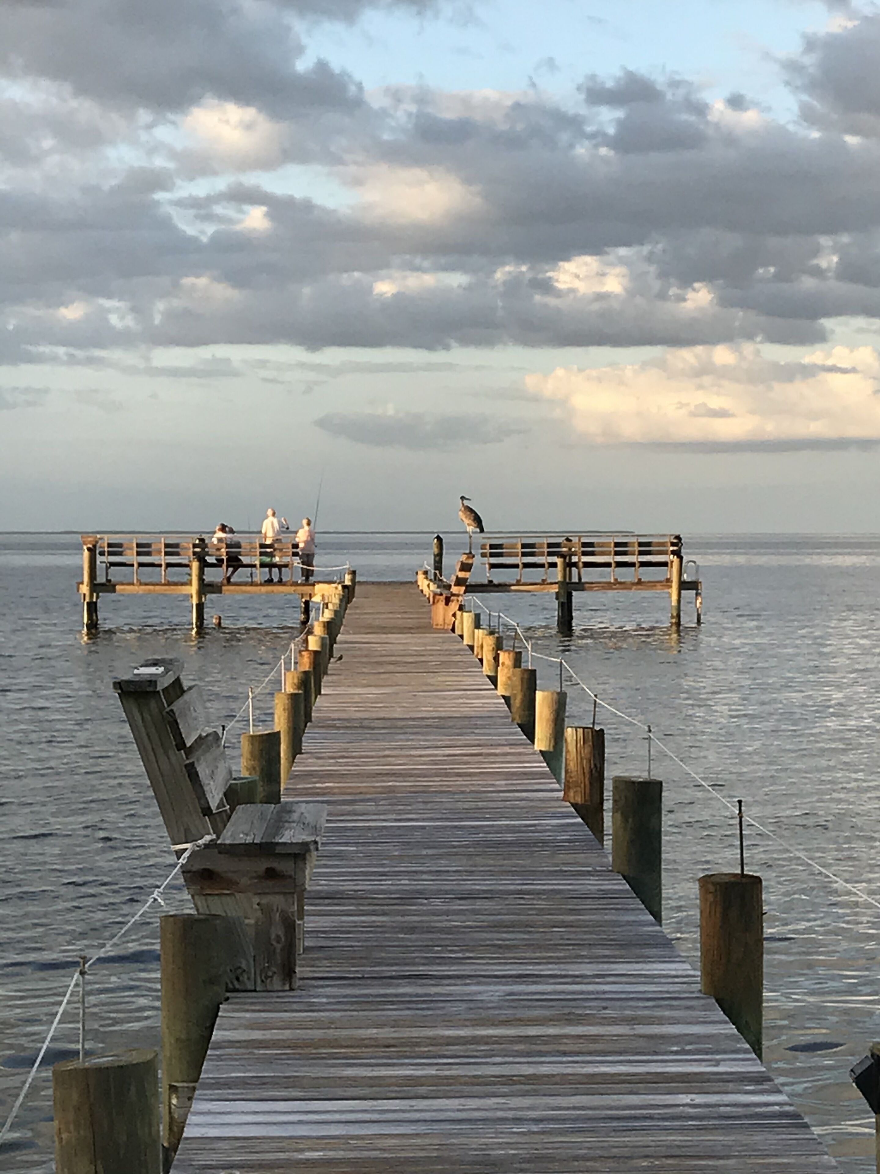 A wooden pier extending into calm water, with benches and people fishing.